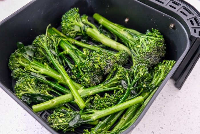 raw broccolini placed in black air fryer tray on white counter
