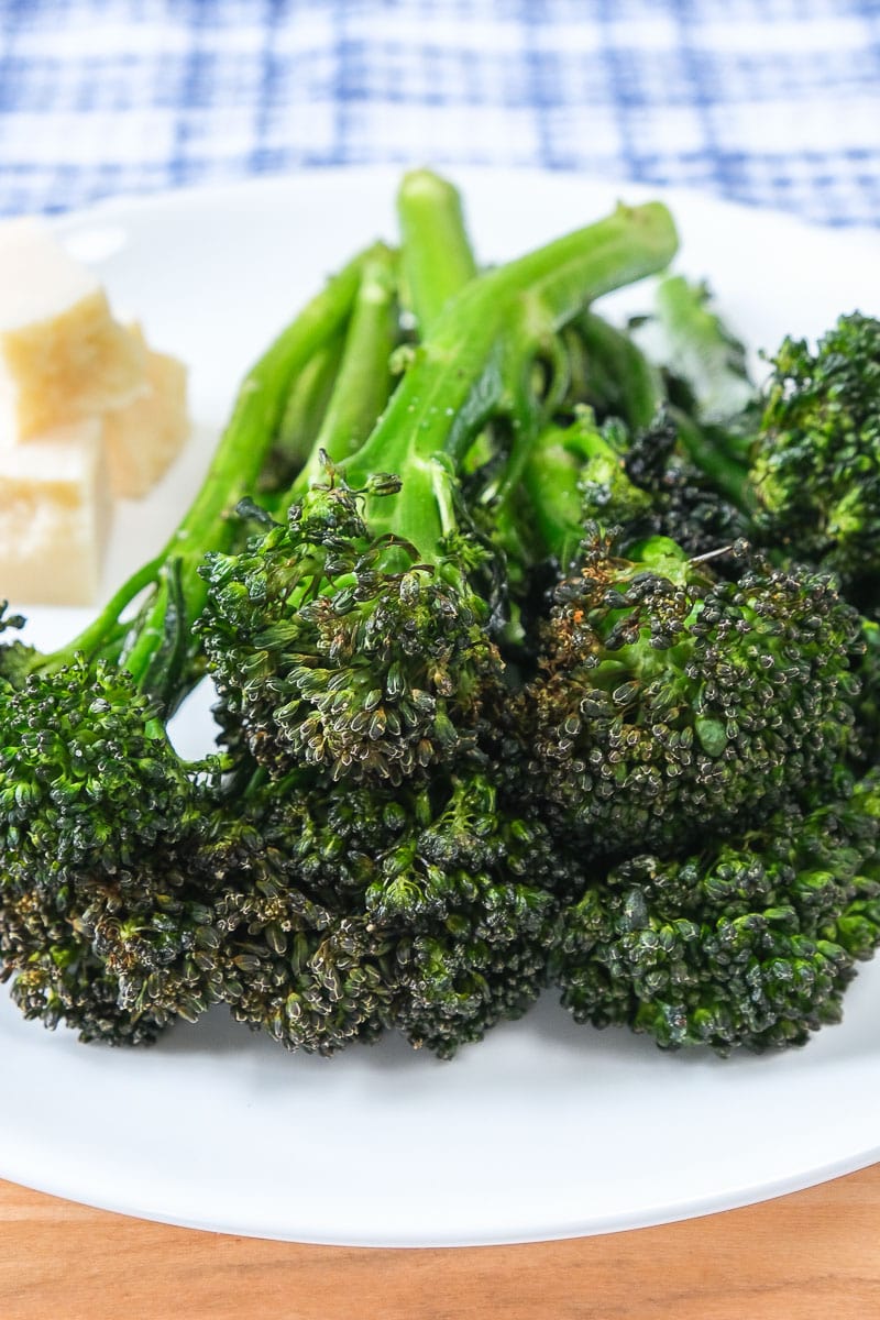 green broccolini on white plate with wooden board underneath