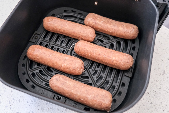 raw chicken sausages in black air fryer tray on white counter