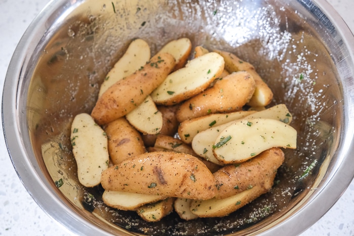 raw fingerling potatoes in metallic bowl with oil and spices