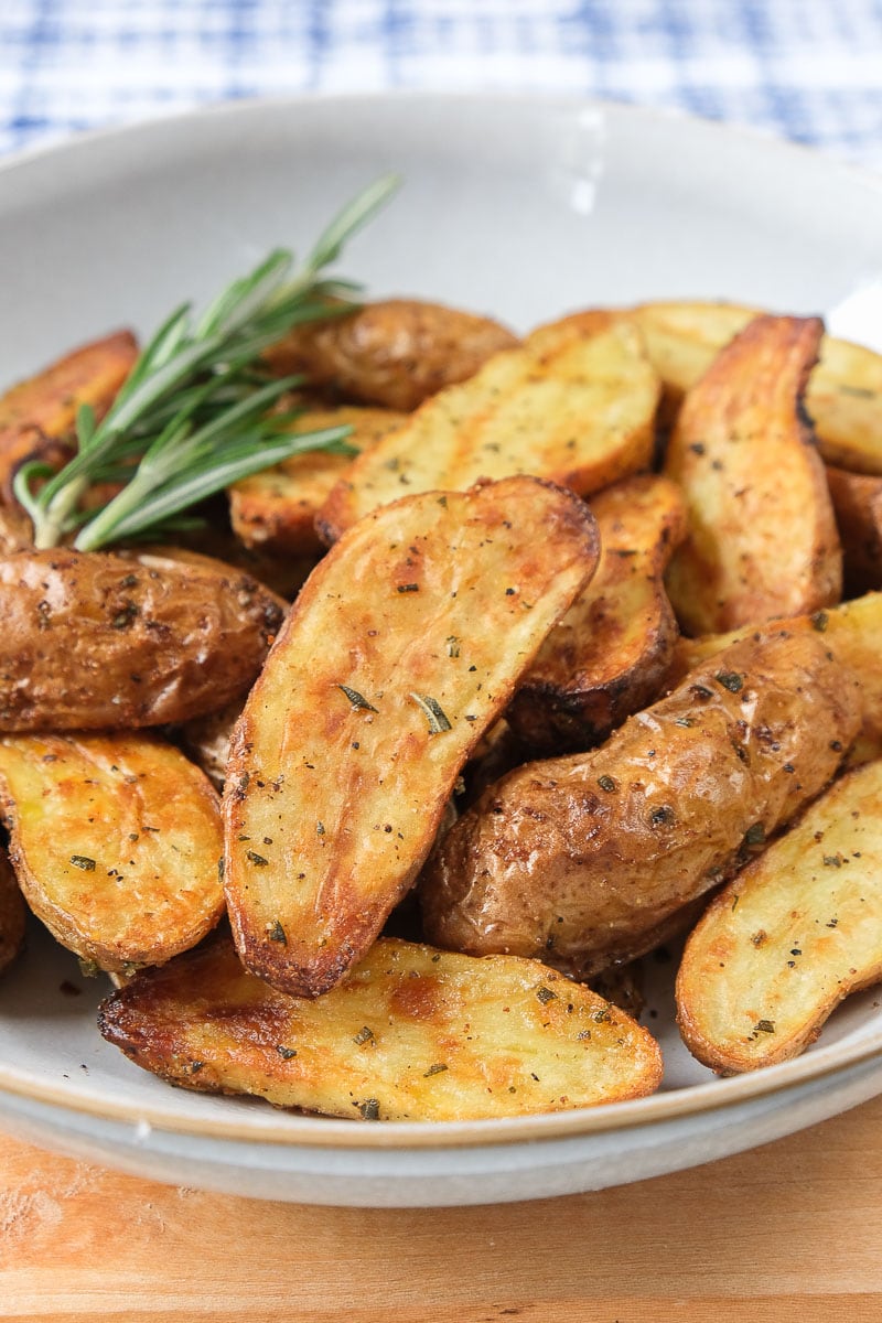 crispy fingerling potatoes with rosemary in bowl on wooden board