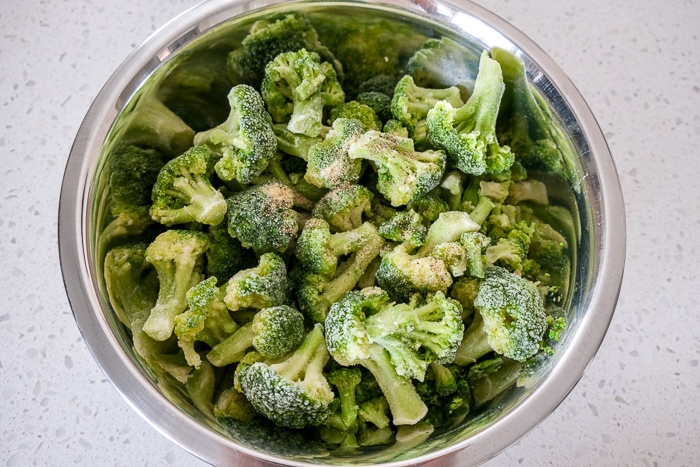 silver bowl of frozen broccoli on white counter top