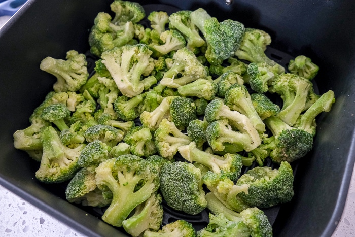 frozen broccoli in black air fryer tray on white counter