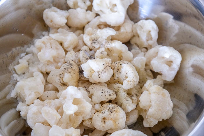 frozen cauliflower in silver bowl with spices unmixed