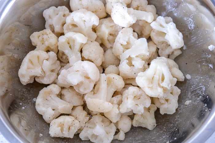 frozen cauliflower in silver bowl covered in oil and spices