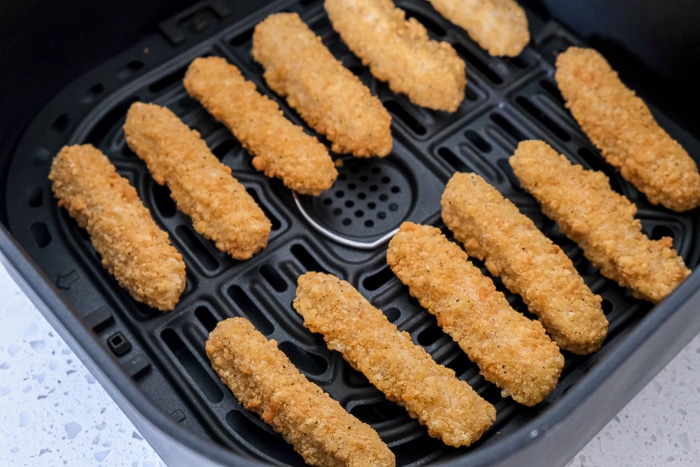 frozen chicken fries in black air fryer tray on white counter