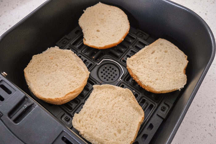 untoasted hamburger buns in black air fryer tray