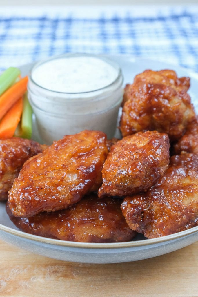 saucy chicken wings in bowl with ranch dip and carrot sticks behind