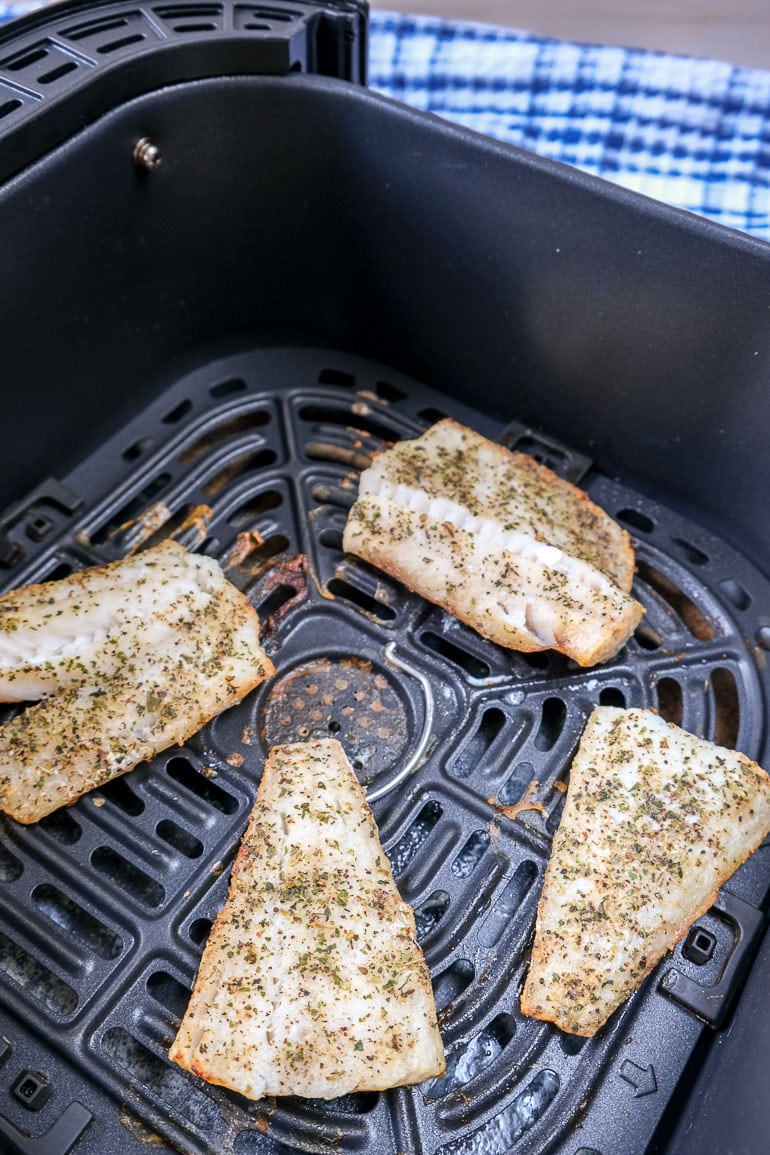 cooked fish fillets in black air fryer tray with blue cloth behind