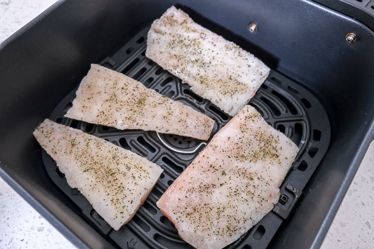 frozen fish fillets in black air fryer tray on white counter