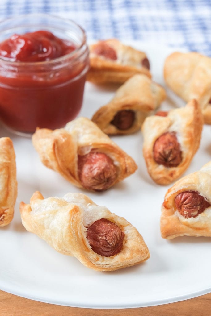 crispy pigs in a blanket on white plate with ketchup for dipping behind