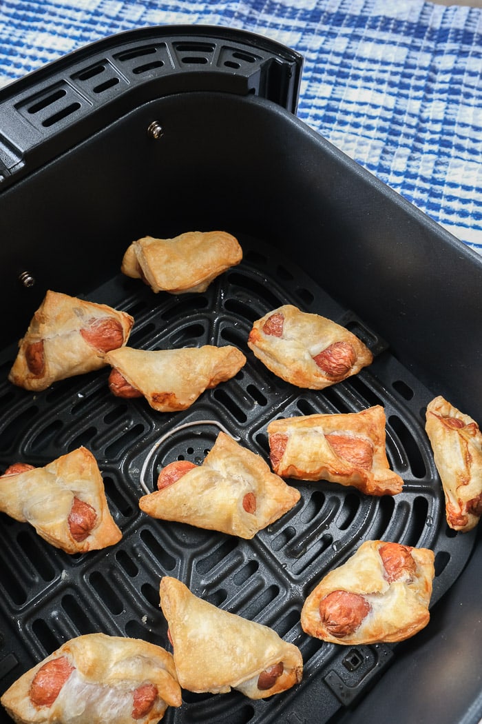 crispy pigs in blankets in black air fryer tray with blue cloth behind