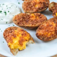 crispy potato skins on white plate with sour cream behind