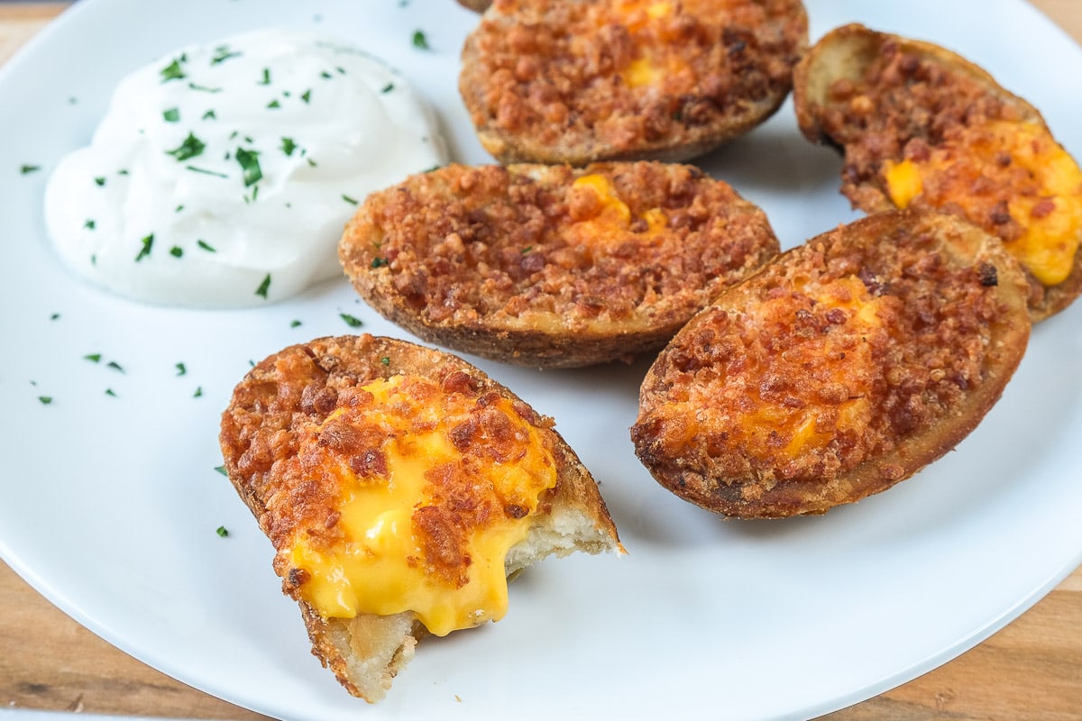 crispy potato skins on white plate with sour cream behind