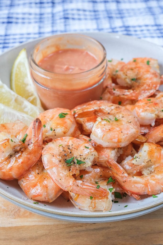 cooked shrimp in bowl with sauce and lemon wedges behind