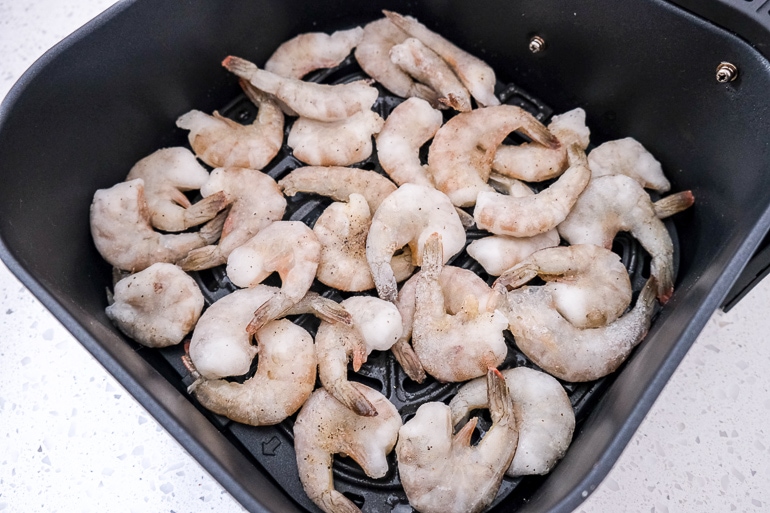 raw shrimp in black air fryer tray on white counter