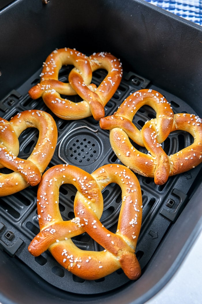 cooked soft pretzels with salt in black air fryer tray on counter