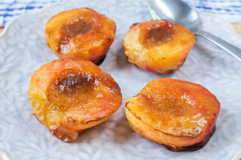 grilled half peaches on floral plate with spoon beside