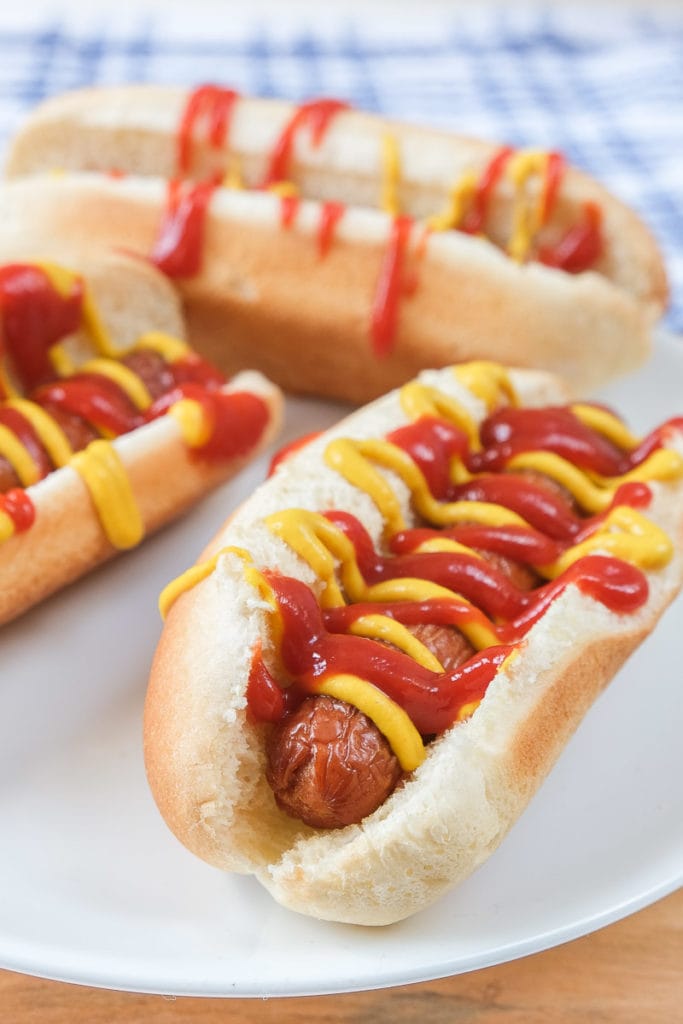hot dogs in buns covered in condiments on white plate