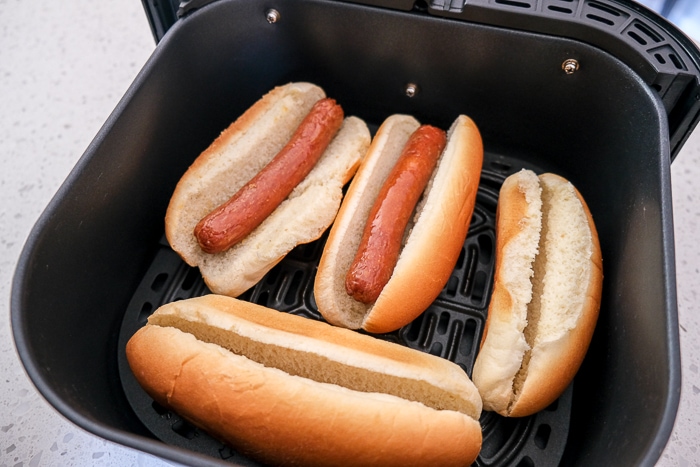 hot dogs in buns in black air fryer tray on counter