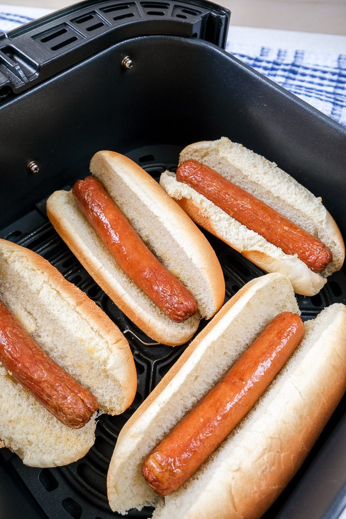 four hot dogs in buns in black air fryer tray