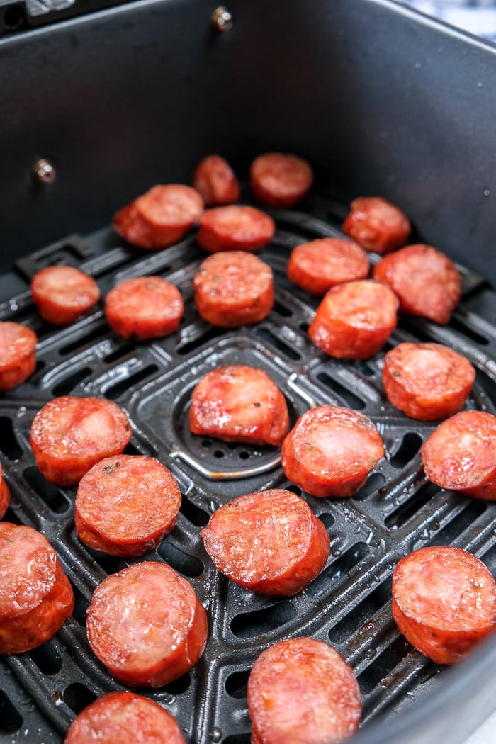 cooked kielbasa pieces in black air fryer tray on counter