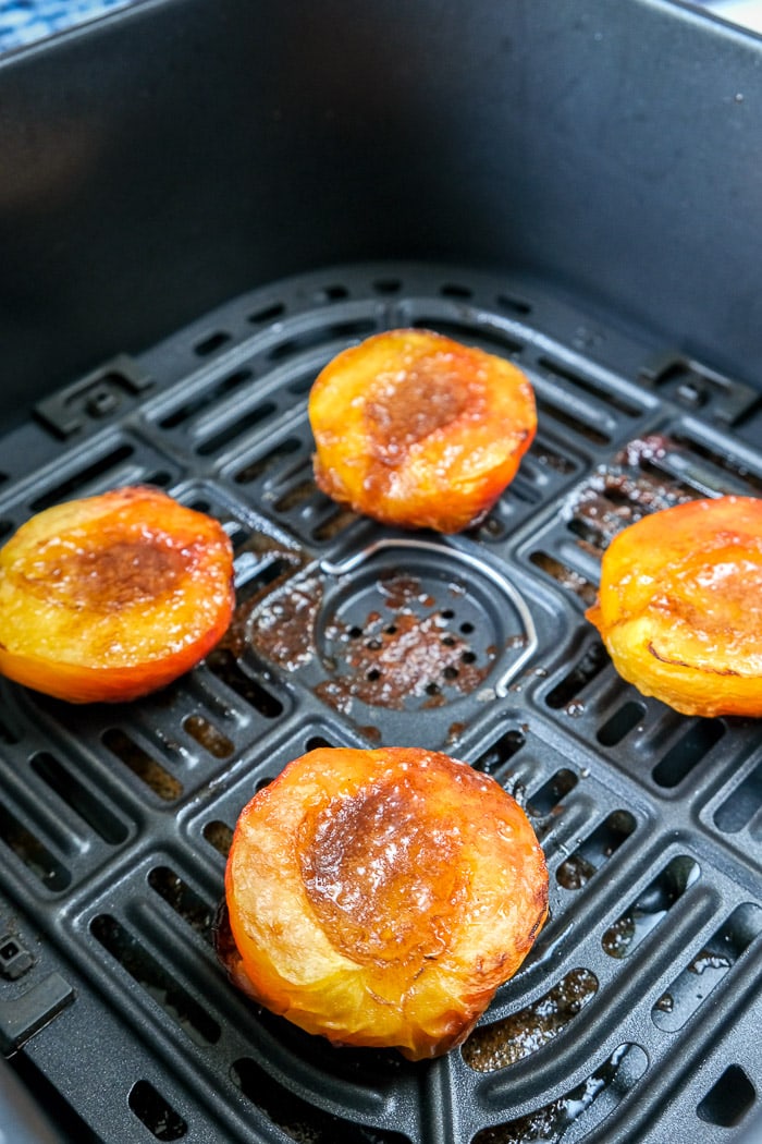 peaches with sugar and butter on top in black air fryer tray