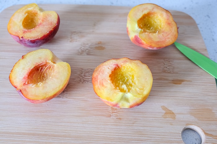fresh peaches cut in half on wooden cutting board