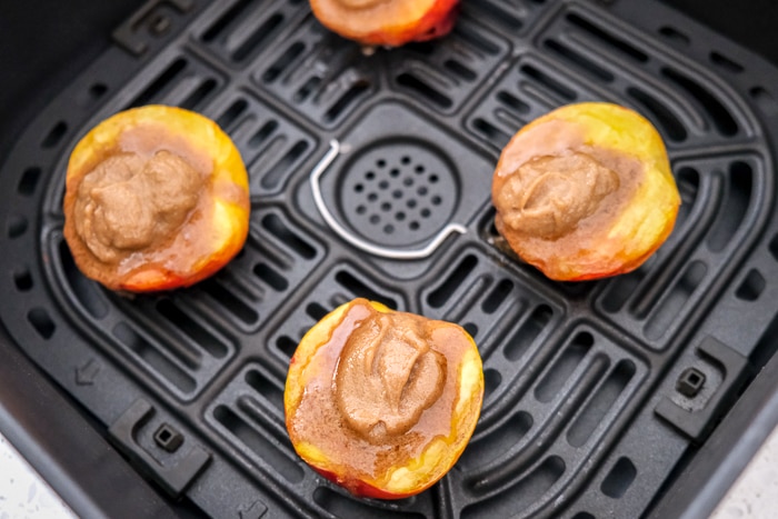 grilled peaches in air fryer tray with sugar butter mixture on top