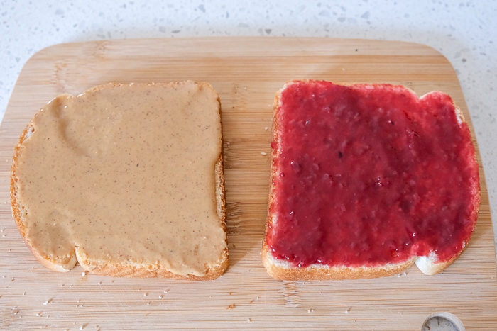 slices of white bread on cutting board with peanut butter and jam spread on top