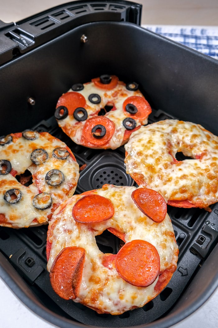 cooked pizza bagels in black air fryer tray on white counter top