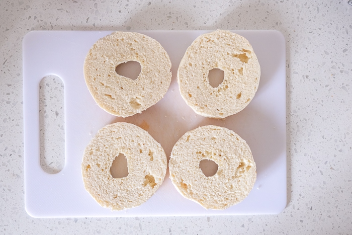 four half bagels cut open on white cutting board on counter