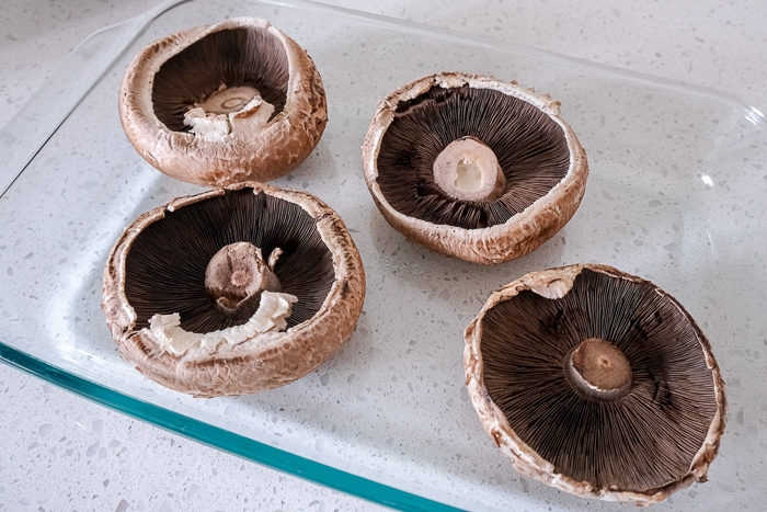 raw portobello mushrooms in glass baking dish on white counter