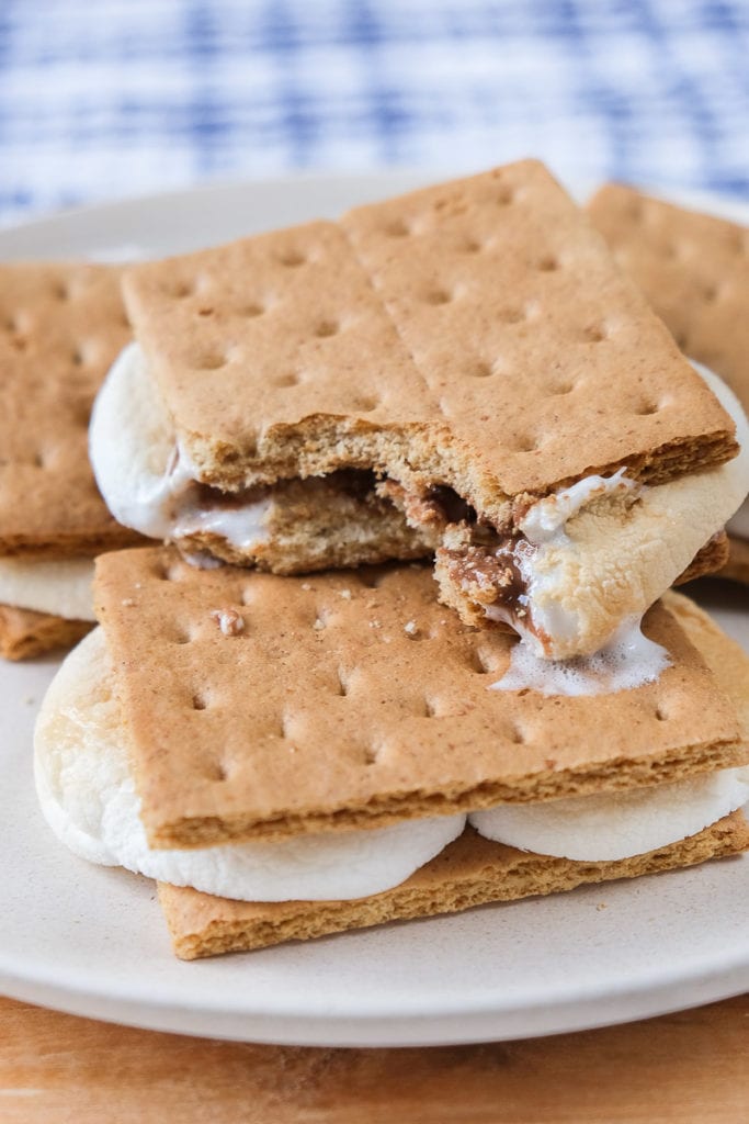 smores with bite out of it on white plate with blue cloth behind