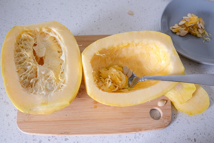 silver spoon scooping seeds out of spaghetti squash on wooden board
