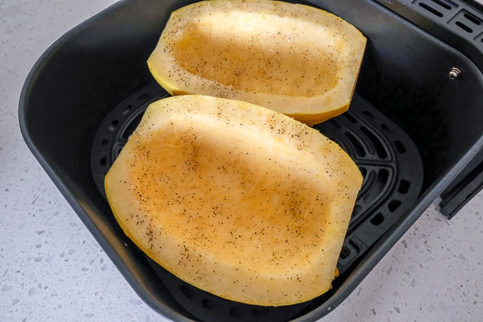 halves of spaghetti squash in black air fryer tray on white counter