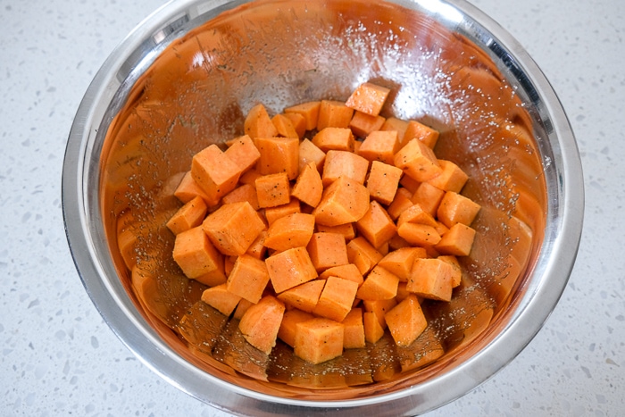 sweet potato cubes tossed in spices and oil in silver bowl