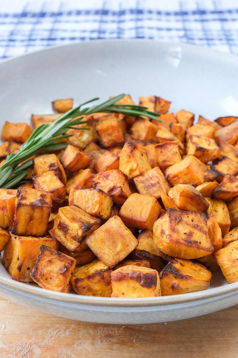 sweet potato cubes in bowl with rosemary behind