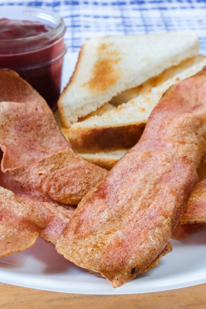 strips of turkey bacon on white plate with toast and jam behind