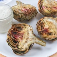 cooked artichoke halves on white plate with dip