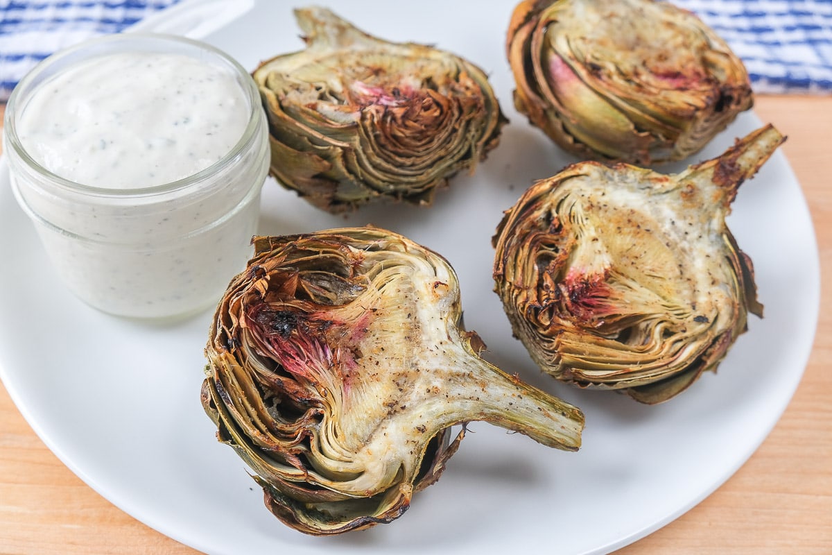 cooked artichoke halves on white plate with dip