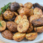 baby potatoes with spices on them and rosemary in bowl on wooden board