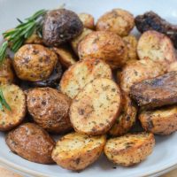 baby potatoes with spices on them and rosemary in bowl on wooden board