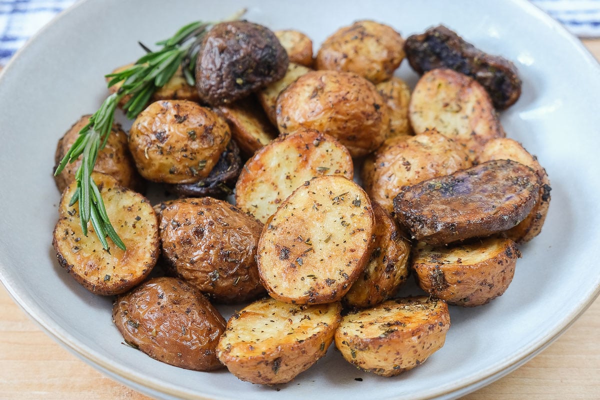 baby potatoes with spices on them and rosemary in bowl on wooden board