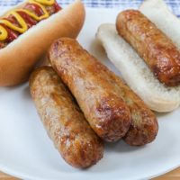 chicken sausages on white plate with buns behind