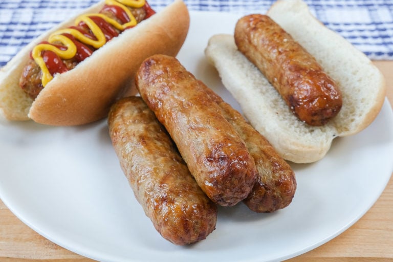 chicken sausages on white plate with buns behind