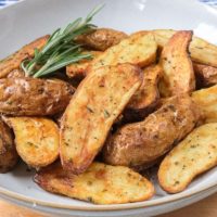 crispy fingerling potatoes in bowl with rosemary on wooden board