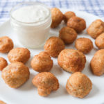 battered mushrooms on white plate with dipping sauce behind