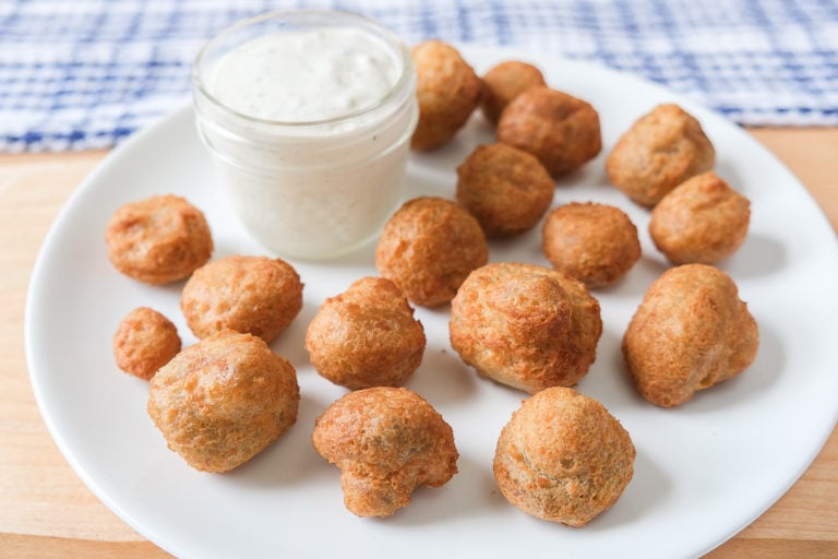 battered mushrooms on white plate with dipping sauce behind