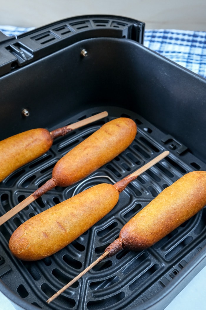 cooked corn dogs in black air fryer tray on counter